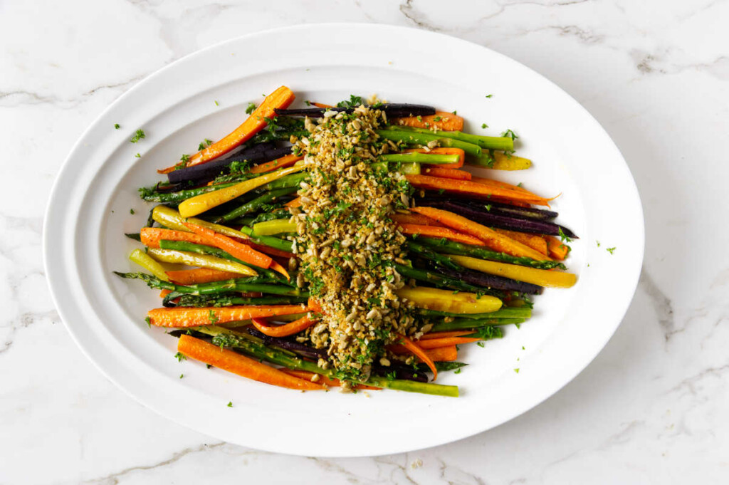 Rainbow carrots and asparagus on a white platter with sunflower seed gremolata.