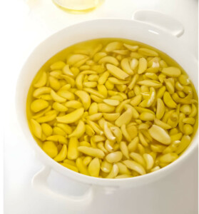 Adding pre peeled garlic cloves to a baking dish with olive oil.