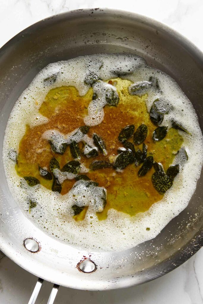 A skillet filled with sage brown butter on a white counter.