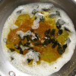 Crispy leaves of sage in brown butter sauce in a skillet.
