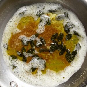Crispy leaves of sage in brown butter sauce in a skillet.