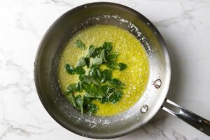 Adding sage leaves to a skillet with hot butter.