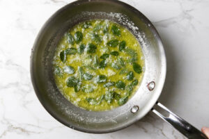 Sage leaves sizzling in hot butter on a skillet.