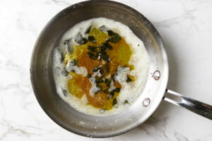 Crisp sage leaves in brown butter sauce in a metal skillet.