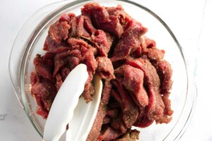 Tossing strips of sliced steak in seasoning.