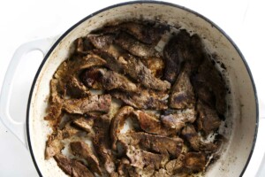 Sliced browned beef strips in white cast iron skillet.