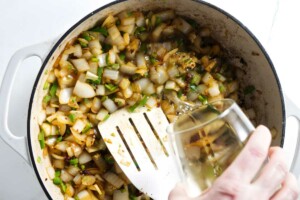 Pouring wine into a skillet with sautéed onions.