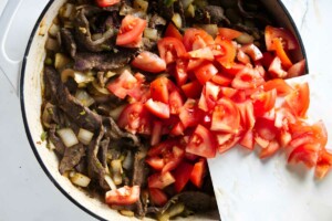 Adding tomatoes to the skillet with the steak strips.