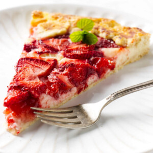 A fork next to a slice of strawberry cream cheese galette on a white plate.