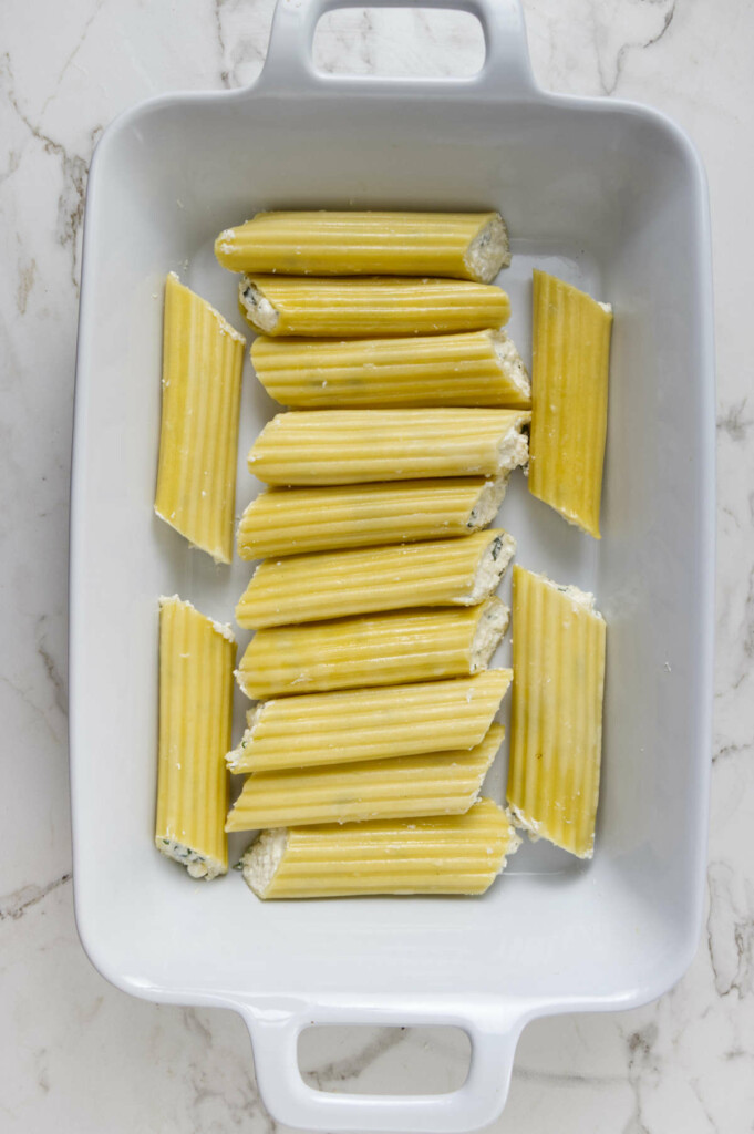 Fourteen stuffed manicotti arranged in a 13x9-inch baking dish, ready to be baked for a cheesy Italian comfort food dinner.
