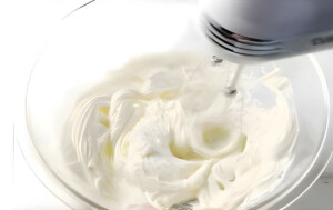 Whipping white ganache in a mixing bowl with a mixer.