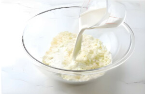 Pouring hot cream over chopped white chocolate in a bowl.
