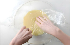 Covering white chocolate ganache in plastic wrap to let it rest.