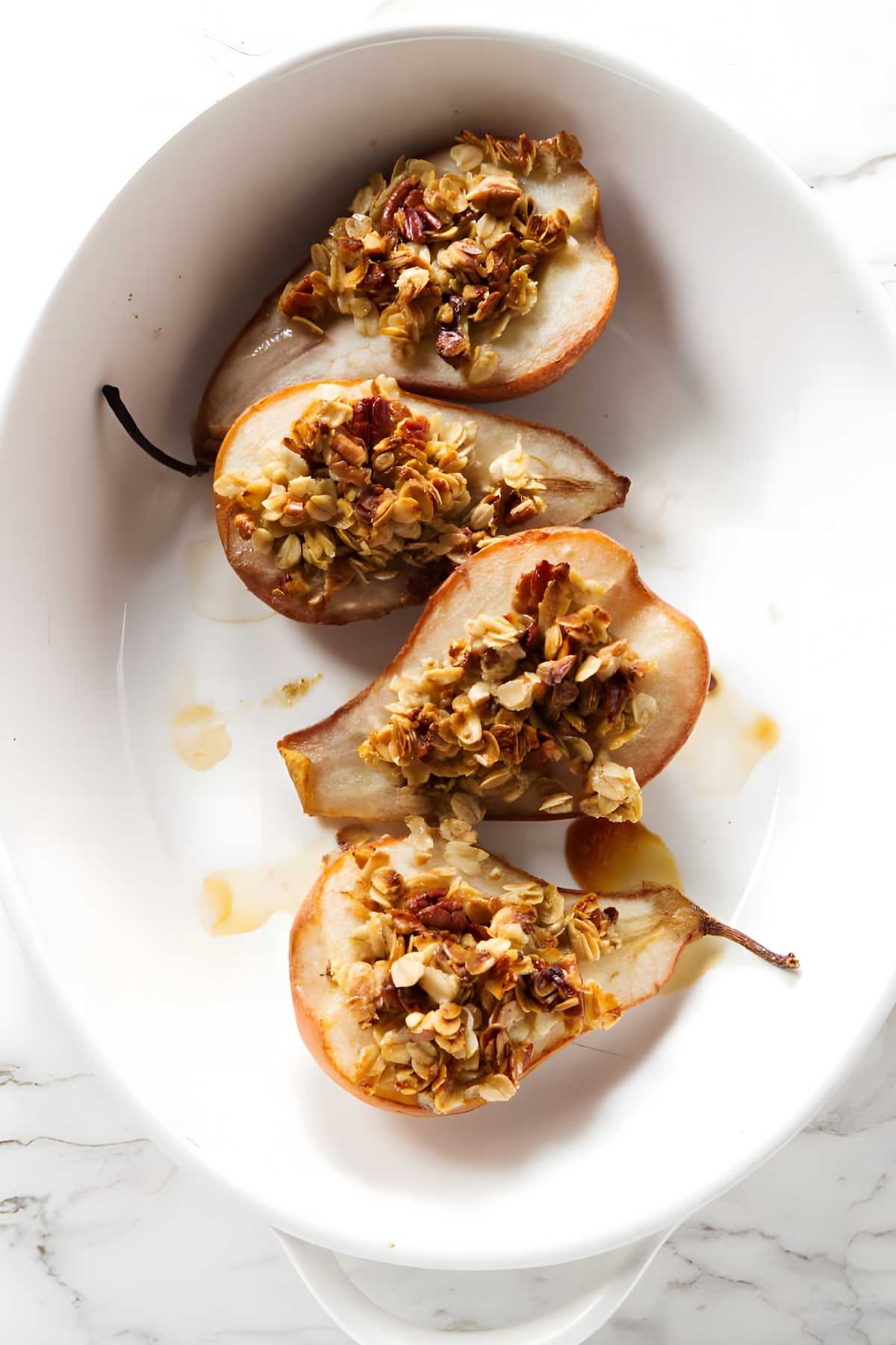 Halved baked pears with oat nut crumble in a white dish.