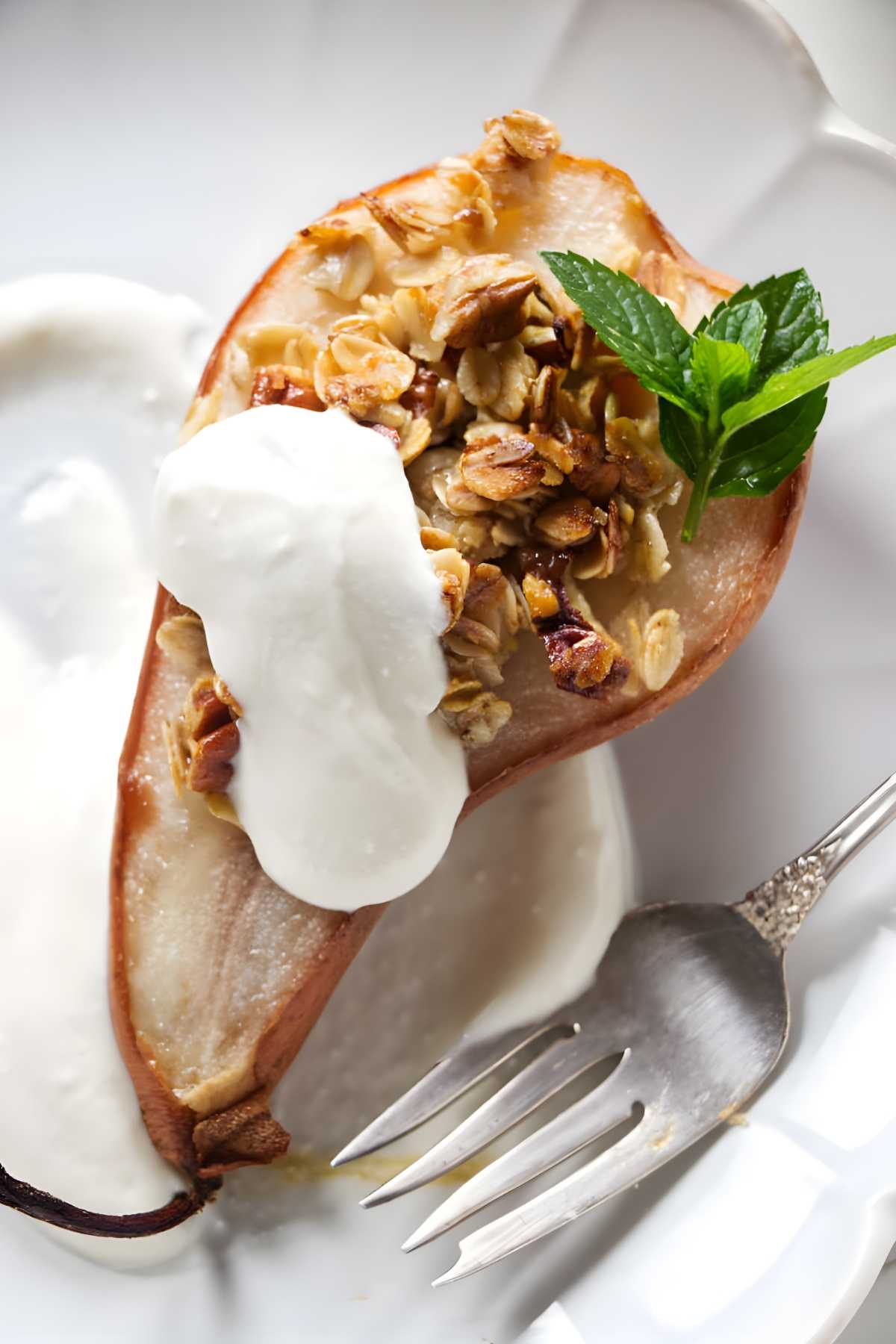 Baked pear with granola, whipped ricotta, mint garnish on white plate.