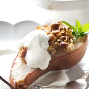 Baked pear with granola, nuts, yogurt, and mint on a plate.
