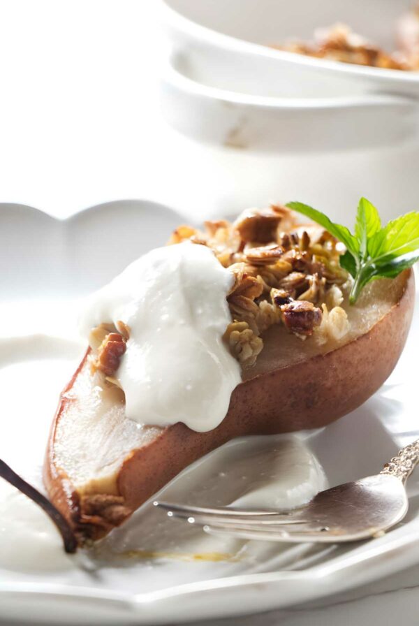 Baked pear with granola, nuts, yogurt, and mint on a plate.