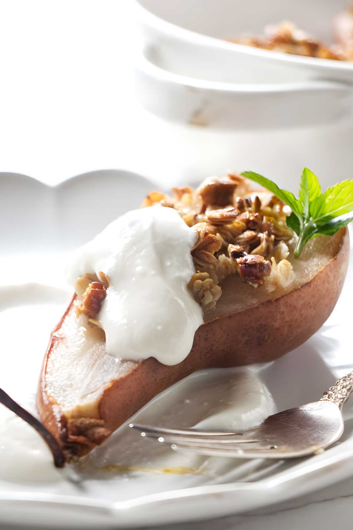 Baked pear with granola, nuts, ricotta, and mint on a plate.