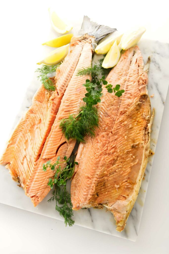 A baked salmon with tail, garnished with herbs and lemon wedges.