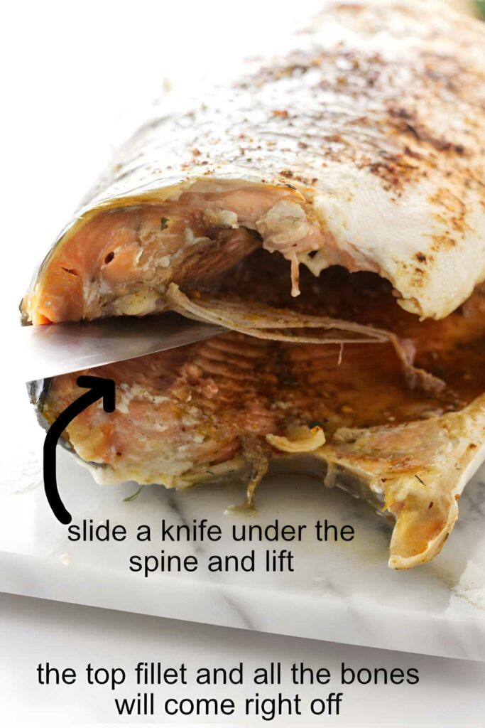 Cooked whole salmon with knife under spine; instructional filleting text displayed.