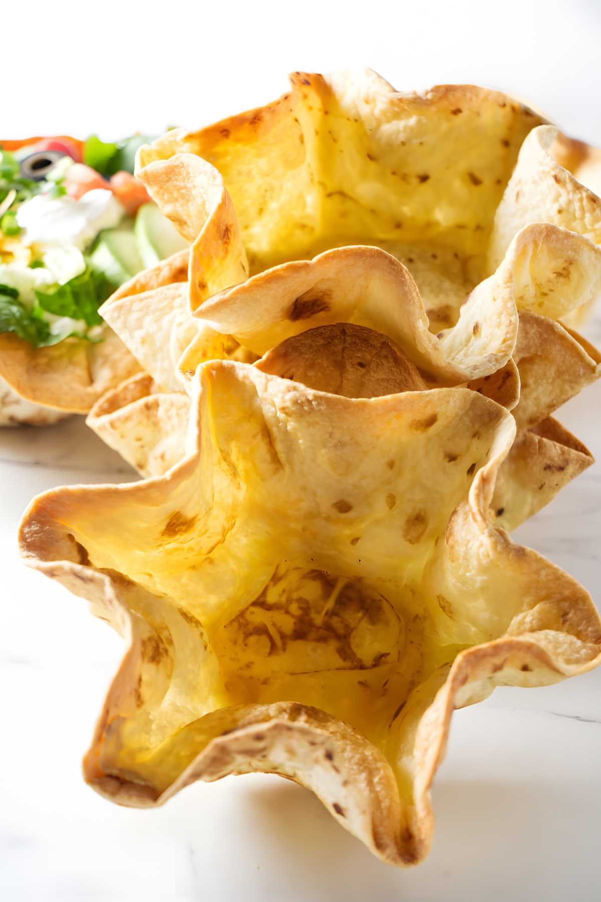 Stacked empty tortilla bowls, with a filled salad bowl in the background.