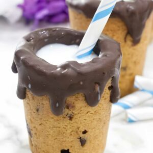 Cookie cup with chocolate, milk, straw; more cups and flowers behind.