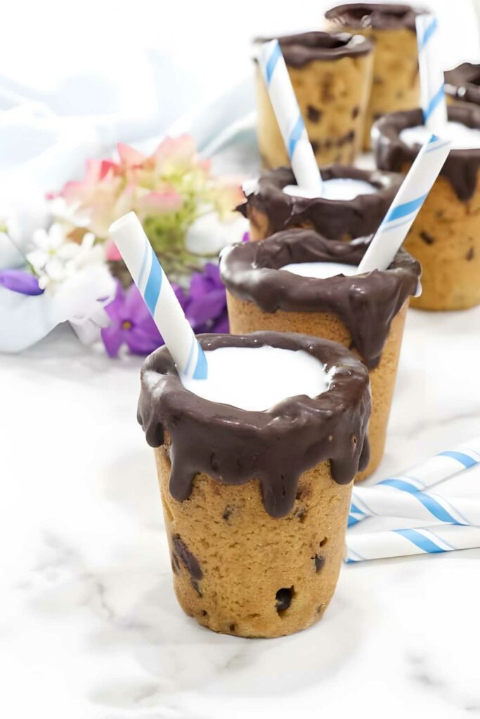 Chocolate cookie cups with milk and straws, flowers in the background.