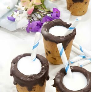 Chocolate chip cookie cups with milk and straws; flowers in background.