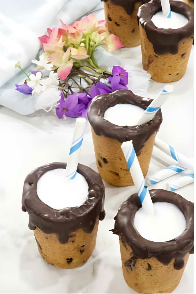 Chocolate chip cookie cups with milk and straws; flowers in background.