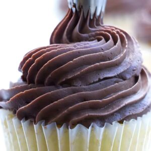 Close-up of chocolate frosting piped onto a vanilla cupcake in white liner.