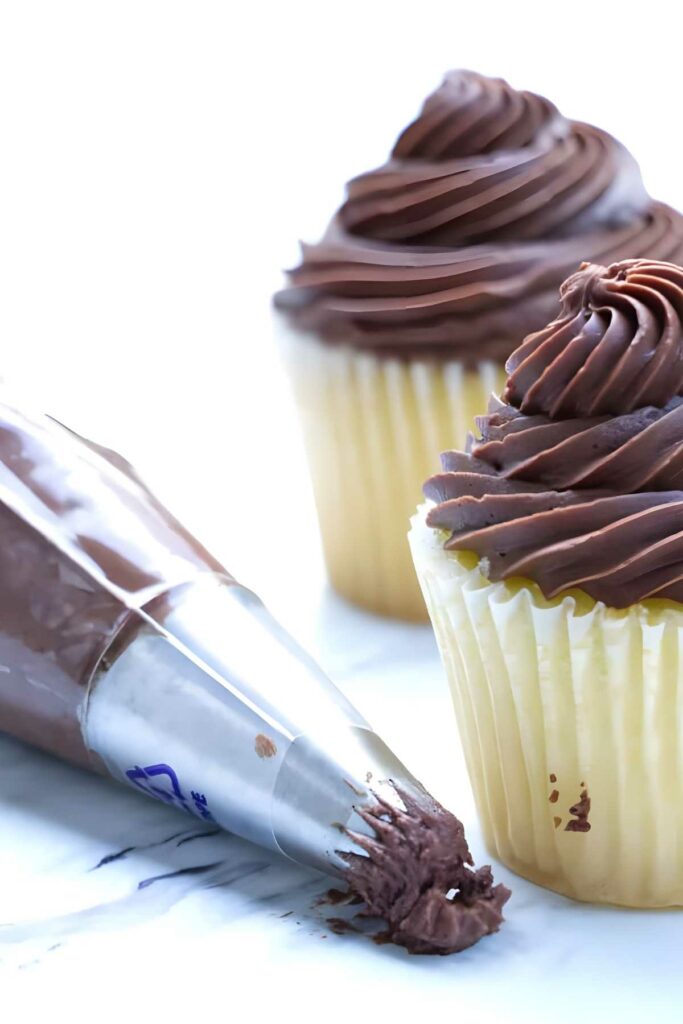 Piping bag and two chocolate-frosted vanilla cupcakes.