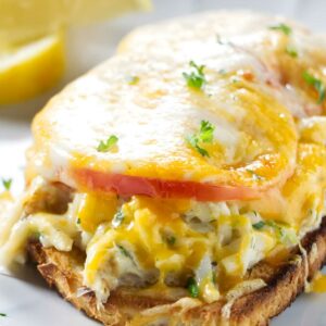 Open-faced crab sandwich with melted cheese, tomato on toasted bread.