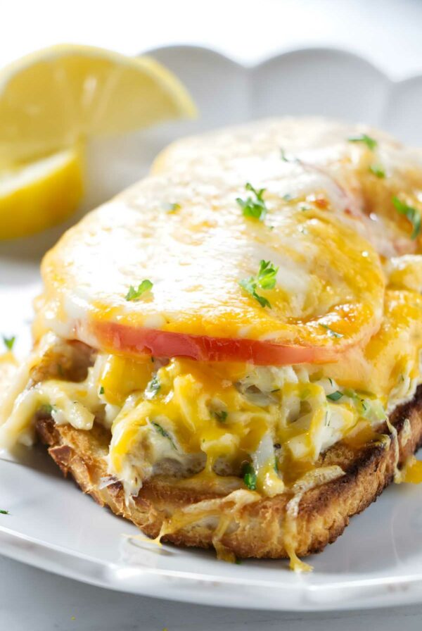 Open-faced crab sandwich with melted cheese, tomato on toasted bread.