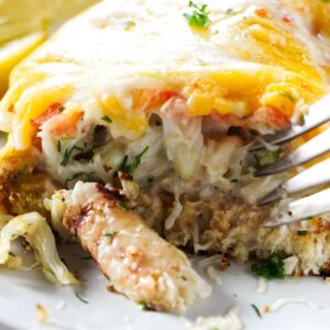 Close-up of cheesy crab casserole with herbs, lemon slices, and fork.