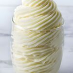 Clear glass of swirled white cream with decorative peaks, blurred background.