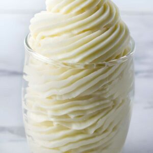 Clear glass of swirled white cream with decorative peaks, blurred background.