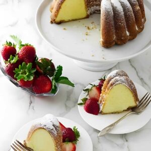 Pound cake bundt cake with strawberries, some slices plated, on marble surface.