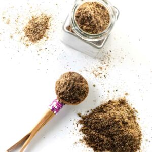Wooden spoon, spice jar, and scattered ground spice on white surface.