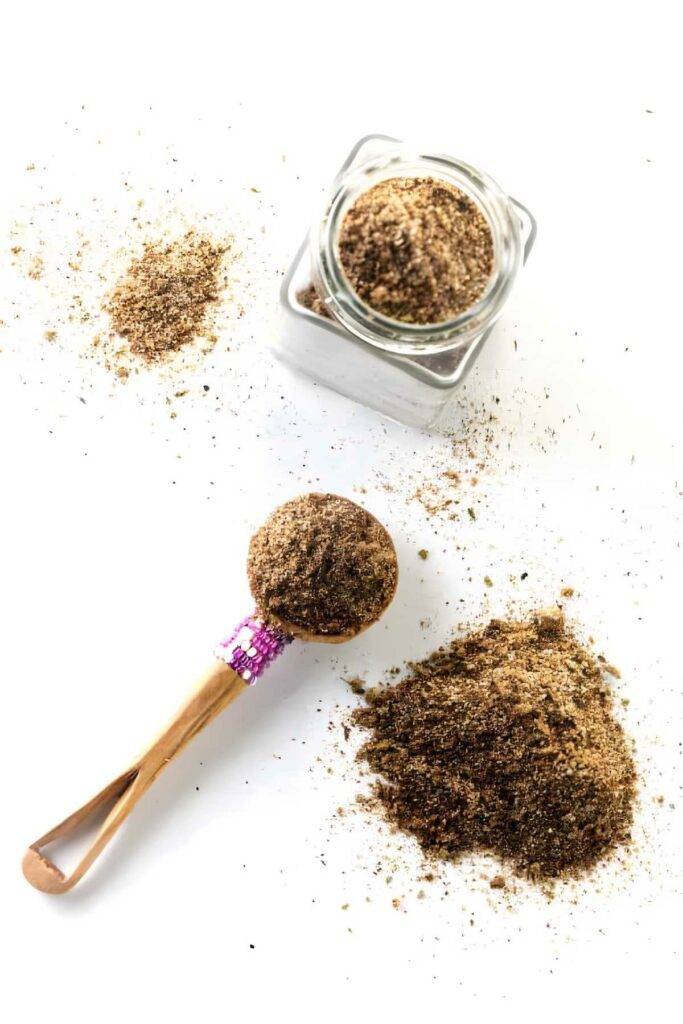 Wooden spoon, spice jar, and scattered ground spice on white surface.