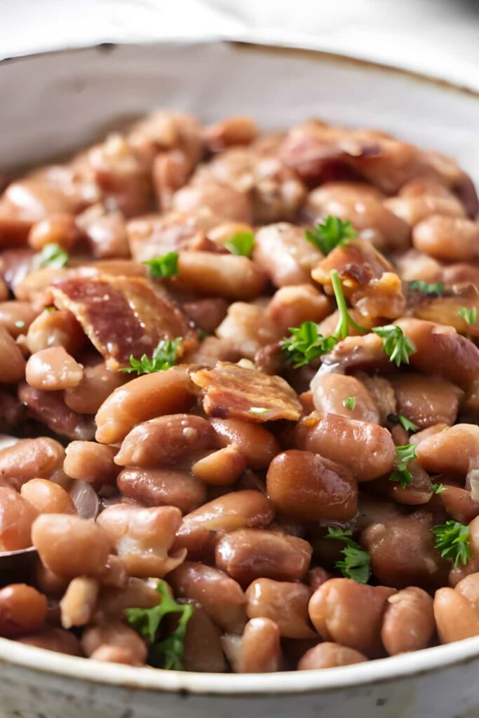 Close-up of cooked pinto beans with bacon and parsley garnish in bowl.