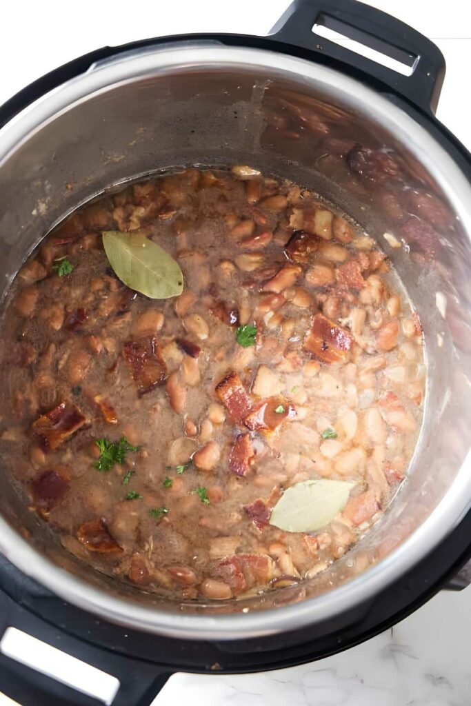 Cooked beans with bacon, bay leaves, and herbs in Instant Pot.