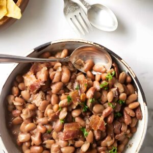 Bowl of pinto beans with bacon, parsley; tortilla chips beside.