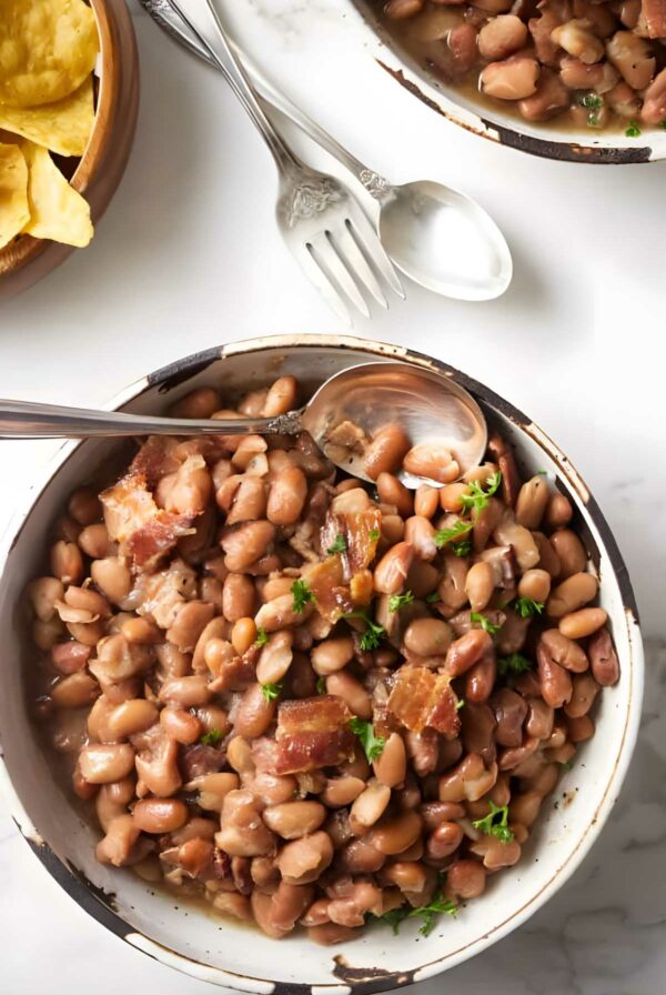 Bowl of pinto beans with bacon, parsley; tortilla chips beside.