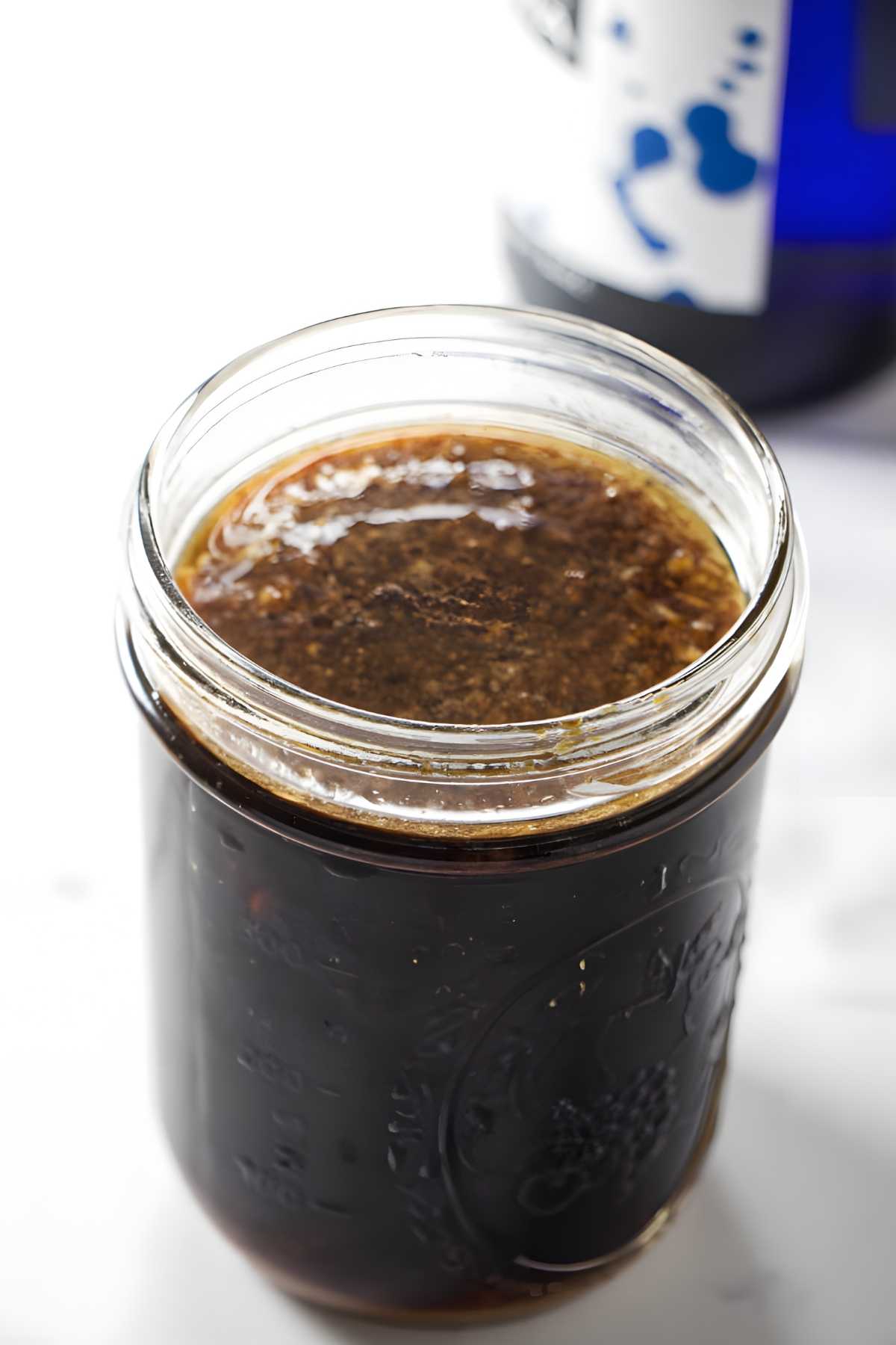 Close-up of jar with dark brown sauce and seasonings, bottle blurred behind.