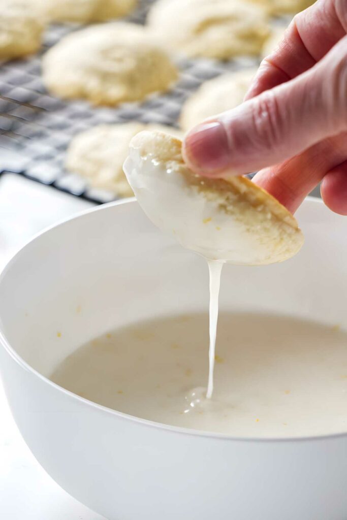 Hand dipping round cookie in white icing.