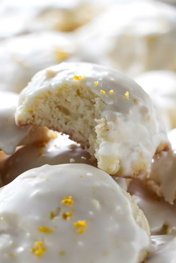 Glazed lemon ricotta cookies topped with zest; one bitten, showing soft inside.