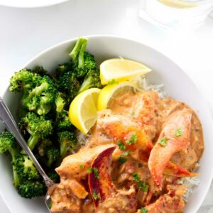 Lobster stew over rice with broccoli, lemon wedges, and parsley garnish.