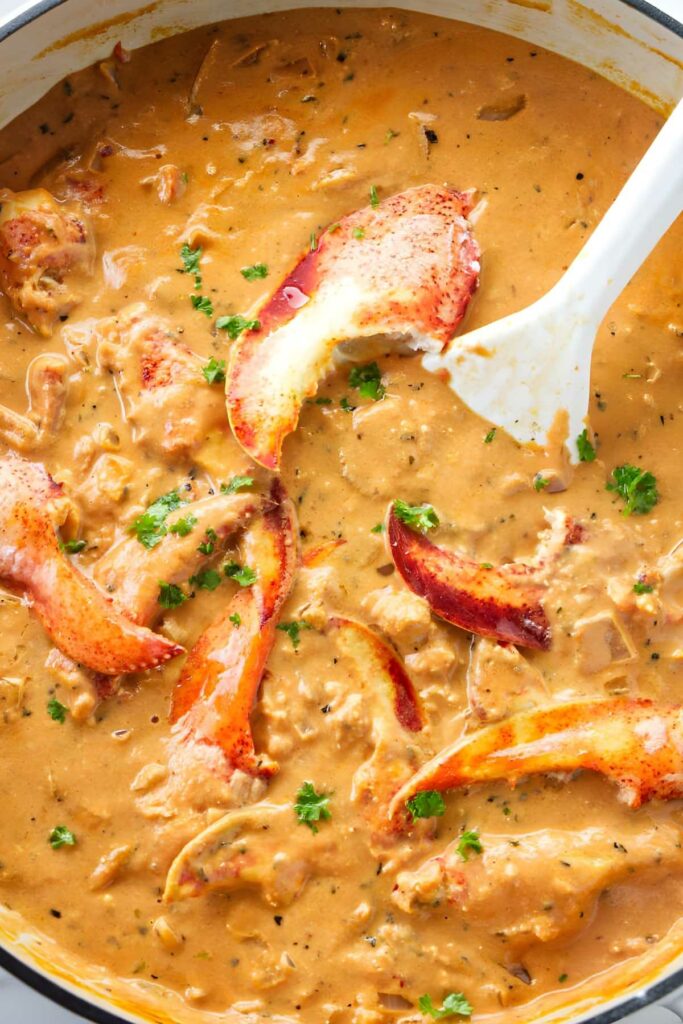 Lobster chunks in a creamy tomato sauce, stirred by white spoon.