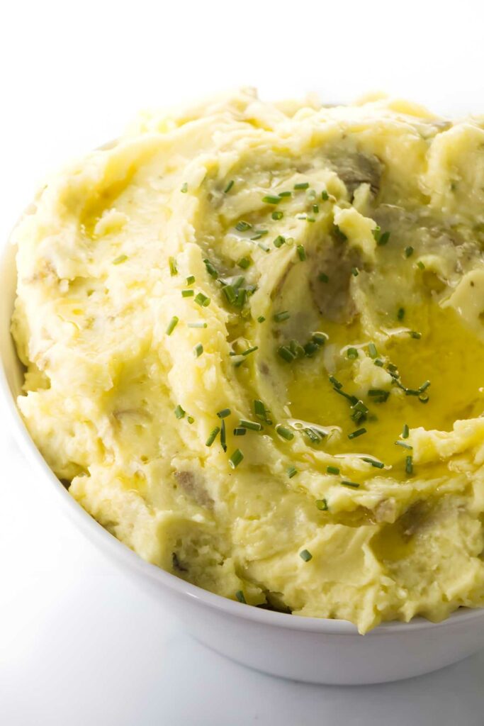 Bowl of mashed creamer potatoes with melted butter and chopped chives on top.