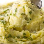 Close-up of mashed potatoes with chives, melted butter, and spoon serving.